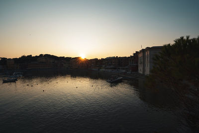 Scenic view of river by buildings against sky during sunset