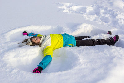 High angle view of smiling teenage girl relaxing on snow covered field