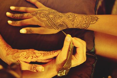 Cropped image of woman drawing henna tattoo on hand