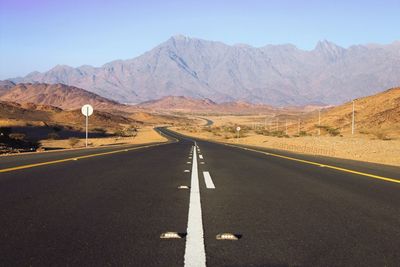 Road leading towards mountains against clear sky