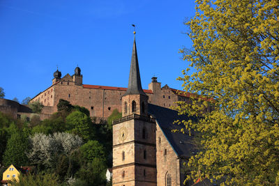 Low angle view of trees and buildings against blue sky