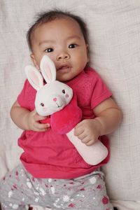 Portrait of cute baby girl with toy lying on bed at home