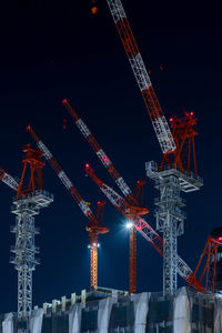Illuminated cranes at construction site against sky at night