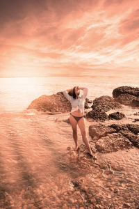 Full length of woman standing on beach against sky during sunset