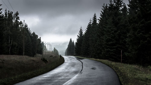 Country road passing amidst trees against cloudy sky