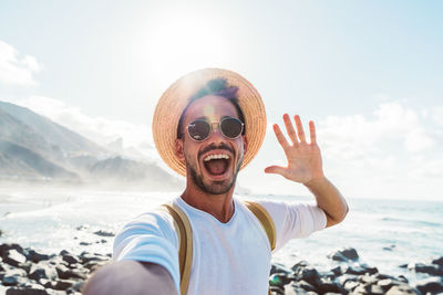 Portrait of man with mouth open waving while standing at beach