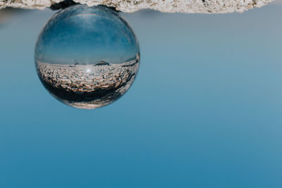 Close-up of upside down crystal ball with reflection against clear sky