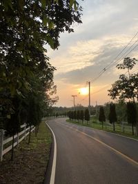 Empty road by trees against sky during sunset