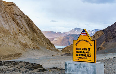 Information sign on rock by mountains against sky