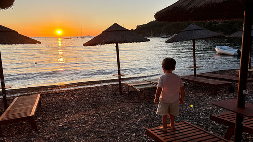 Rear view of man standing at beach against sky during sunset