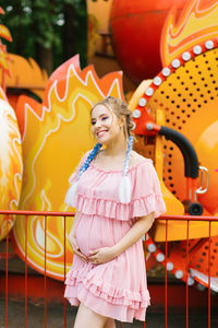 Cheerful pregnant young woman with blue pigtails and bright makeup walks in an amusement park