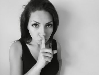 Close-up of young woman with finger on lips against white background