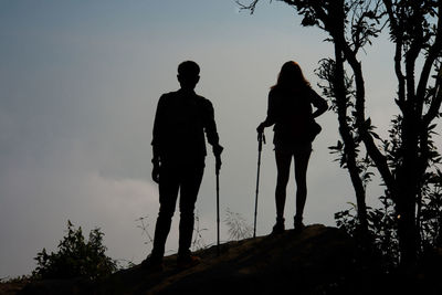 Low angle view of silhouette couple hiking on mountain against sky