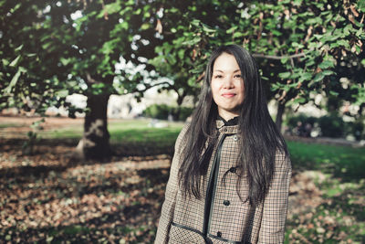 Beautiful middle-aged japanese woman in stylish coat in autumn park, smiling. sunlight, copy space