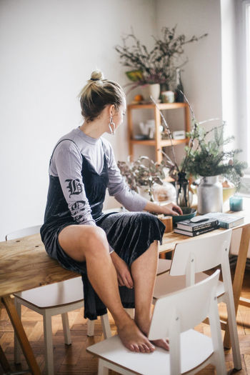 FULL LENGTH OF WOMAN SITTING ON TABLE AT HOME