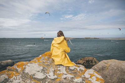 France, brittany, landeda, dunes de sainte-marguerite, young woman sitting on rock at the coast