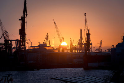 Cranes at commercial dock against sky during sunset