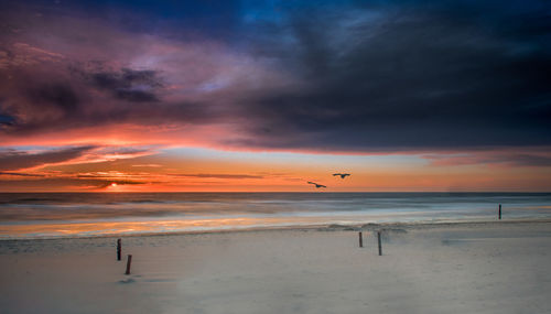 Scenic view of beach against cloudy sky during sunset