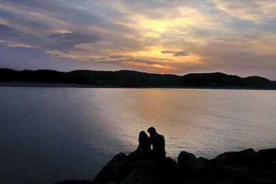 Friends sitting on rock against sky during sunset