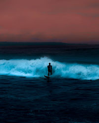 Man surfing on sea against sky during sunset