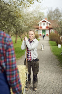 Smiling teenage girl looking at father carrying hay in wheelbarrow on footpath