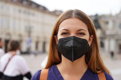 Student girl wearing a protective kn95 ffp2 black mask looking at camera with urban background