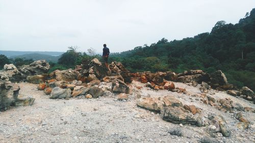 Rear view of man standing on rock against sky