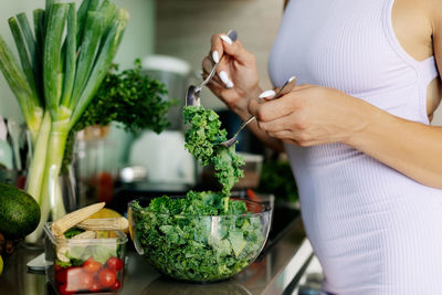 Close-up of a woman's hand stirring lettuce leaves in a glass bowl while cooking a healthy meal.