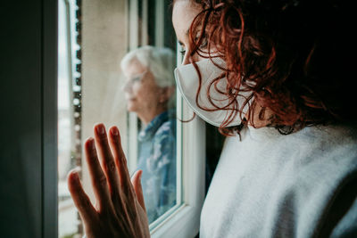 Portrait of woman looking through window at home