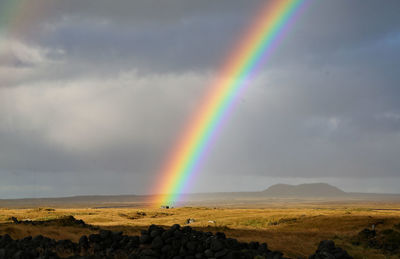 Scenic view of rainbow over landscape against cloudy sky