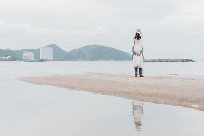 Newlywed couple standing on beach against sky