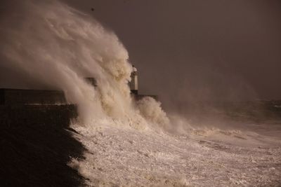 Scenic view of sea waves splashing on pier against sky