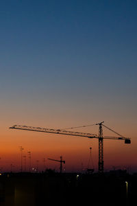 Silhouette cranes at construction site against clear sky during sunset