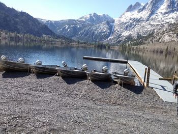 Boats moored in lake by snowcapped mountains against sky