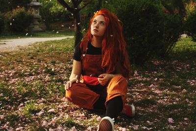 Full length of young woman looking up while flowers falling on land