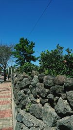 Stone wall by trees against clear blue sky