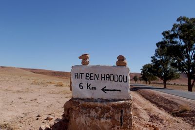 Sign board by road against clear blue sky