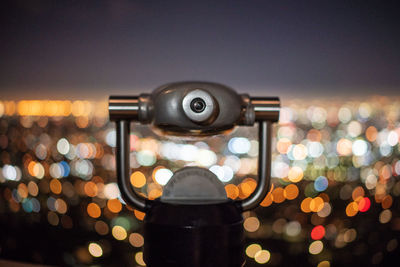 Close-up of coin-operated binoculars against illuminated cityscape