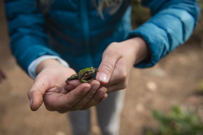 Midsection of girl holding frog while standing outdoors