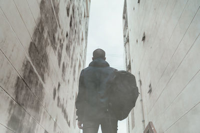 Rear view of man standing by wall against building