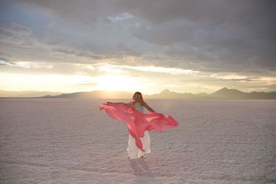 Woman with dupatta standing on desert against cloudy sky