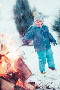 Full length of boy standing by campfire in forest during winter