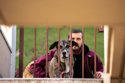 Portrait of dog and a man by camera against wall