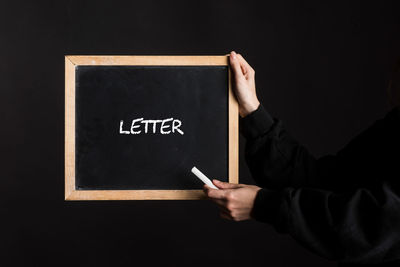 Midsection of man holding blackboard against black background