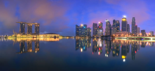 Illuminated buildings by river against sky