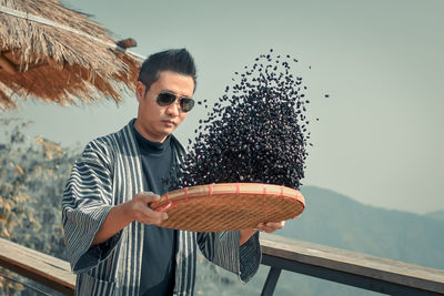 Portrait of young man wearing sunglasses standing against sky