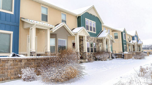 Snow covered houses by buildings against sky