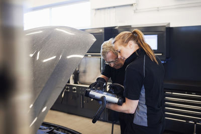 Mechanics using technology while examining car in shop