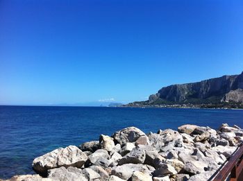 Rocks by sea against clear blue sky