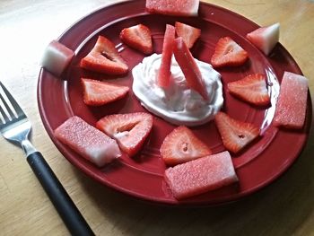 High angle view of sliced fruits with whipped cream in red plate on table